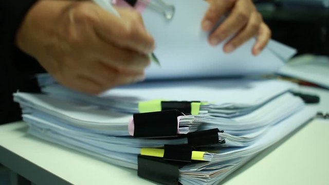 Businessman Preparing reports papers with graphs, charts on Stacks of documents files for finance in office. Piles of unfinished document achieves with paper clip. Concept of Business Annual Report.