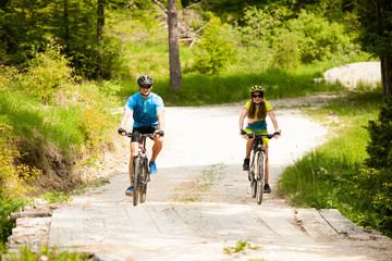 Obraz premium ACTIVE Young couple biking on a forest road in mountain on a spring day