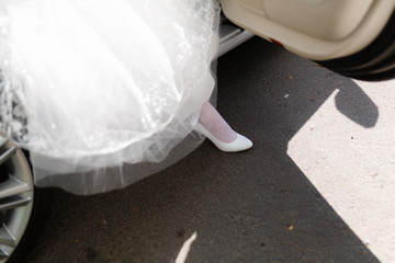 Closeup of woman's legs while she walks to the car. Girl in a dress and white shoes comes out of an expensive car.
