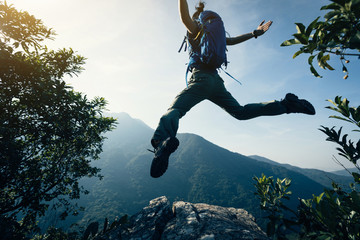 successful female backpacker jumping on cliff's edge