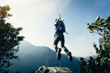 successful young woman backpacker jumping on cliff's edge