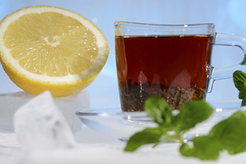 glass cup of strong black tea on a beautiful blue ice with yellow lemon and green mint
