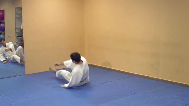 A man in a kimono demonstrates a somersault through himself in the gym. Man doing aikido.