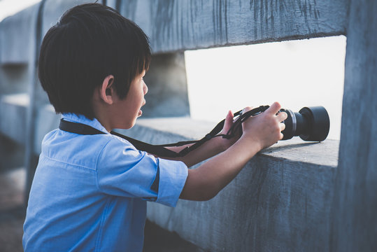 Cute Asian boy taking photo by digital camera outdoors