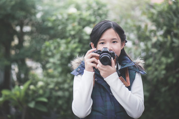 Beautiful Asian girl  in warm clothes with retro  camera shooting a photo in the park