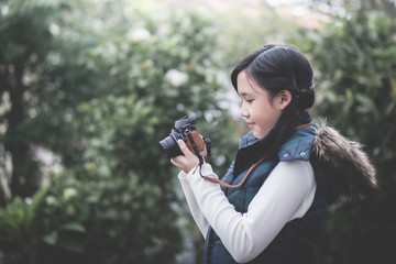 Beautiful Asian girl  in warm clothes with retro  camera shooting a photo in the park