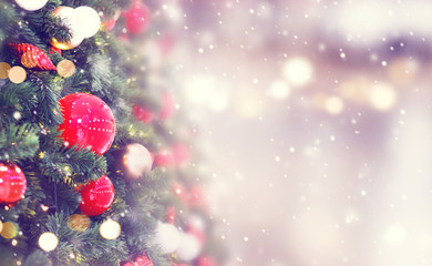 Christmas holiday background. Red bauble hanging from a decorated on christmas tree with bokeh and snow, copy space.