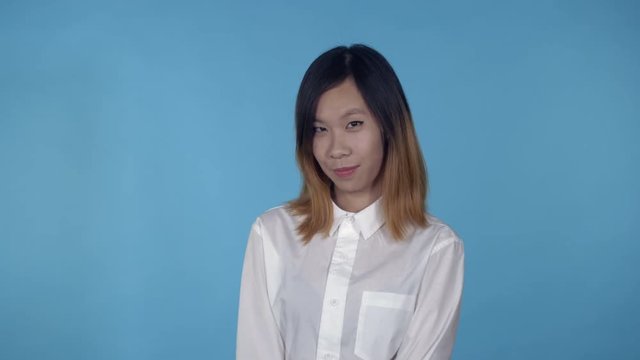young asian woman posing flirting on blue background in studio. attractive millennial girl wearing white casual shirt looking at the camera smiling