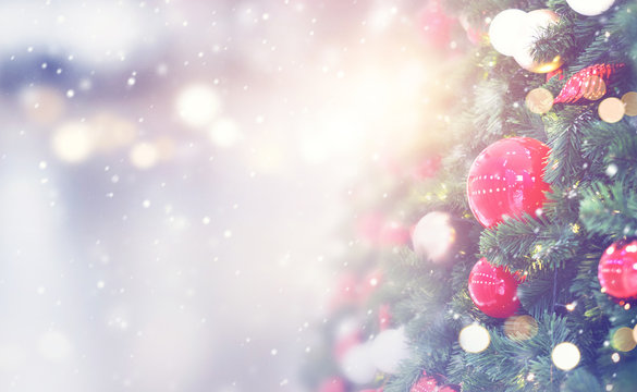 Christmas holiday background. Red bauble hanging from a decorated on christmas tree with bokeh and snow, copy space.