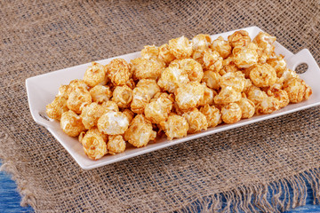 Popcorn with caramel on a white ceramic dish on sacking on a blue wooden background