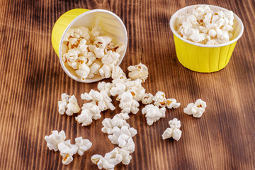 Falling popcorn in yellow paper box on wooden background