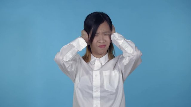 young asian woman posing showing hand gesture loud sound on blue background in studio. attractive millennial girl wearing white casual shirt looking at the camera