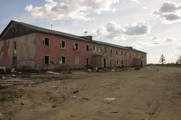 Old two-storied destroyed red house in autumn with sand around. Poverty and misery, North
