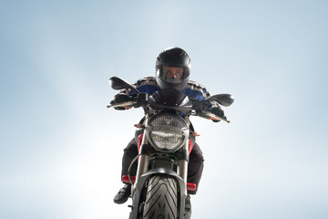 Fototapeta premium Biker in black jacket and helmet sitting on his sportive bike on blue background
