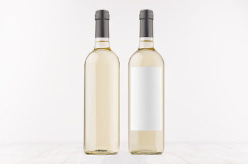 Two transparent wine bottles with blank white label and without label, on white wooden board, mock up. Template for advertising, design, branding identity.