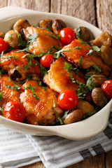 Chicken thighs roasted with chestnuts and tomatoes close-up in a bowl. vertical
