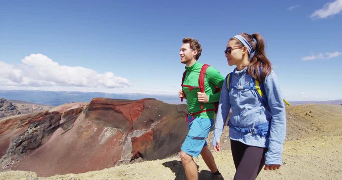 Young couple hiking on nature trek in mountains on sunny day. Male and female backpackers walking in Tongariro National Park, New Zealand. Young people living healthy lifestyle. RED EPIC SLOW MOTION.