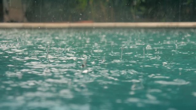 Raindrops fall into the water. Beautiful pool water surface under the rain. Slow motion