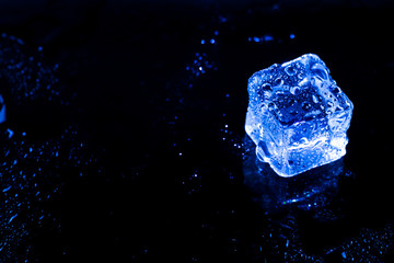 Blue ice cubes on black wet table.