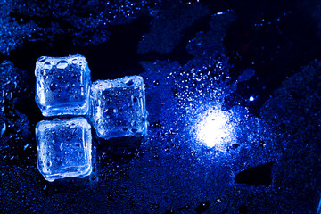 Blue ice cubes on black wet table.