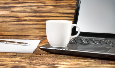 Cup of coffee with laptop and notepad on the wooden table.