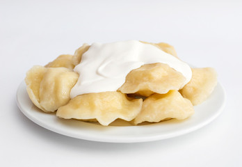 Plate with boiled varenyky and sour cream on white.
