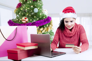 Fototapeta na wymiar Pretty girl holds credit card near Christmas tree
