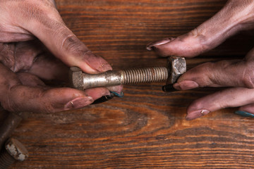Female dirty hands holding a screw nut and a bolt on a wooden background. Dirty job is not a problem for a modern woman