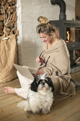 Young beautiful woman in the living room sits on the floor and communicates with friends over the computer, covered with a blanket for the cold in the back of the fireplace