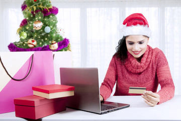 Beautiful woman holds credit card near Christmas tree