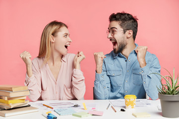 Happy businesspeople clench fists as achieve great results, finishes working on report, look joyfully at each other scream with happiness. Overjoyed female and male students recoice finishing do tasks