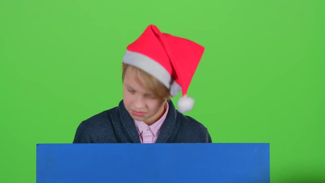 Teenager in a red hat appears from a board on a green screen