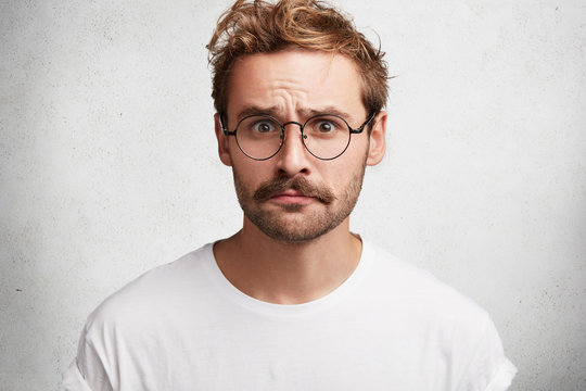 Puzzled indignant male model has mustache and beard, dressed casually, worries to hear bad news about wife`s state of health, isolated over white concrete background. People, reaction, attitude