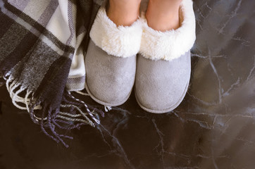 Female legs in cozy slippers on mramor  floor with cashmere blanket. Woman wearing  warm and...