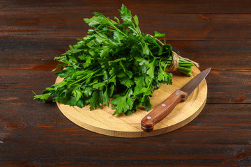 A bunch of green parsley on a wooden table with a knife.
