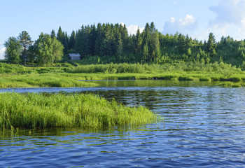 A little hous is on the riverbank. Blue sky reflect in the river water.
