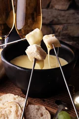 Schilderijen op glas Gourmet Swiss fondue dinner on a winter evening with assorted cheeses on a board alongside a heated pot of cheese fondue with two forks dipping bread and white wine or champagne © beats_