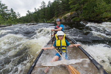 Young boy paddling whitewater in a canoe