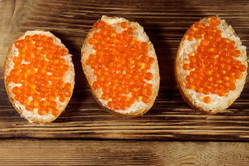 Sandwiches with butter and red caviar on wooden table