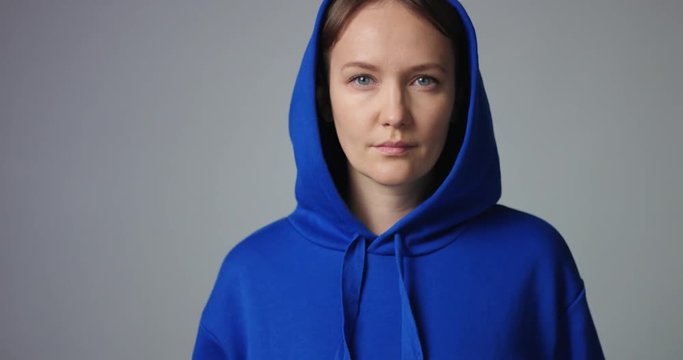 Pretty young woman with short dark hair and bright blue eyes wearing a hoodie walkes into camera focus on white background
