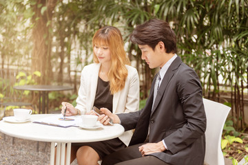 Happy Businessman and businesswoman using a documents together while businessman hand holding mobile phone in the garden, happy business successful concept.