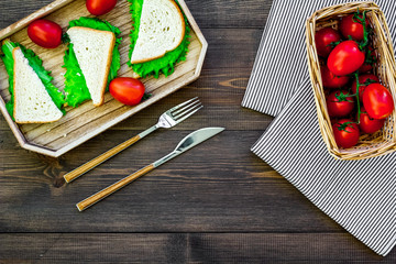 Sandwiches with lettuce and tomatoes for picnic on tablecloth on dark wooden background top view copyspace