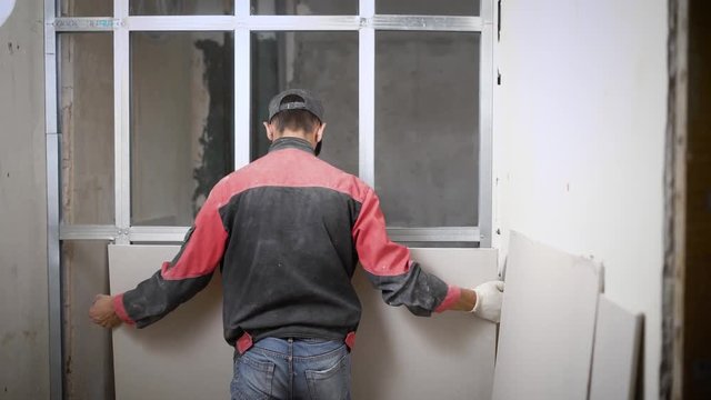Man covering metal construction of wall with panels on building site