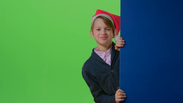 Teen in christmas hat with bubon appears from the side boards on a green screen