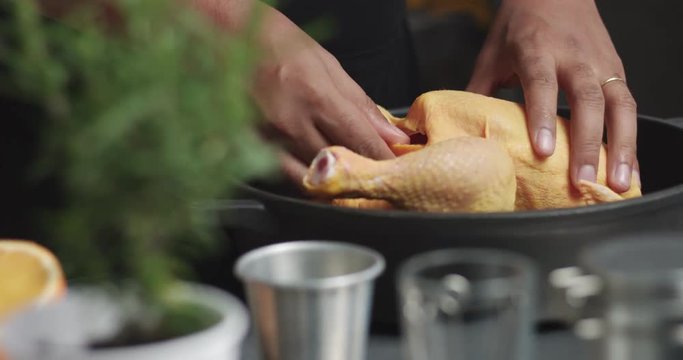 Dark skinned male cook prepares a large chicken for roasting with orange and rosemary