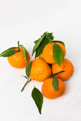 Fresh, ripe, organic mandarin oranges, clementines or tangerines with stems and leaves still wet with water drops on white wooden background, untreated mandarines with little blemishes, freshly picked