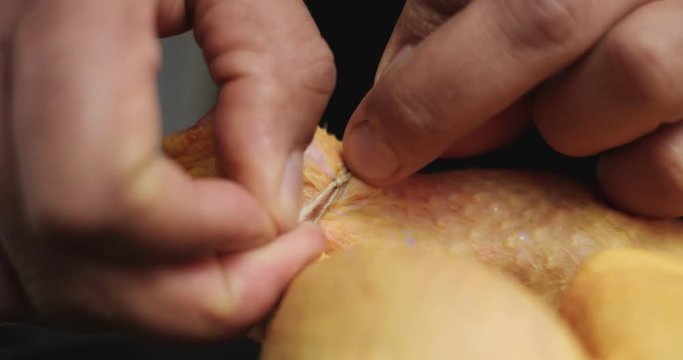 Male cook ties chicken legs for roasting in a black cast iron pan, close up video