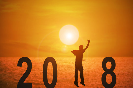 Silhouette of young man jumping on the beach between 2018 years with beautiful sunset at the sea, concepts of news year and business target.
