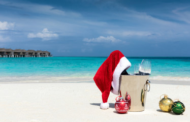 Sekt Kübel mit Weihnachtsmütze und Christbaumkugeln am tropischen Strand auf den Malediven