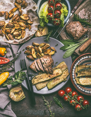 Rustic meal with roasted meat, baked potatoes and vegetables served on plate with cutlery, top view